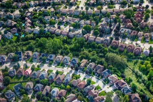 Aerial view of a suburban neighborhood with rows of houses, tree-lined streets, and green yards, from above.